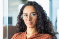 Close-up portrait of confident serious business woman, hispanic woman wearing glasses inside office looking at camera