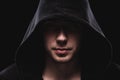 Close-up portrait of a courageous man in a deep dark hood on a black background. The concept of secrecy of secrets and