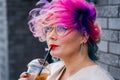 Close-up portrait of curly Caucasian woman with multi-colored hair wearing glasses. The hairstyle model is drinking a
