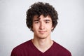 Close up portrait of curly handsome European male, wearing casual maroon shirt, isolated over white background, looking directly