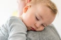 Close-up portrait of cute adorable blond caucasian toddler boy sleeping on fathers shoulder indoors. Sweet little child feeling