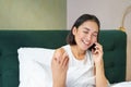 Close up portrait of cute asian girl in bed, talking on mobile phone with happy smiling face. Woman waking up and making Royalty Free Stock Photo
