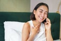 Close up portrait of cute asian girl in bed, talking on mobile phone with happy smiling face. Woman waking up and making Royalty Free Stock Photo