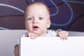 Close-up portrait of cute baby boy in a crib. Adorable open-mouthed baby boy looking at camera Royalty Free Stock Photo