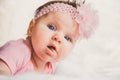 Close-up portrait of cute baby girl in pink lying down on a white bed. Looking at camera. Big open eyes. Healthy little Royalty Free Stock Photo