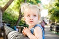 Close up portrait of cute bewildered little blondy toddler girl looking aside up and leaning on a wooden fence in the zoo or city