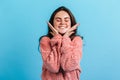 Close-up portrait of cute brunette smiling with eyes closed. Girl in pink sweater gently touches her cheeks. Royalty Free Stock Photo