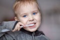 Close up portrait of cute caucasian baby boy with very serious face expression cleaning the teeth with teeth brush, by himself. Br