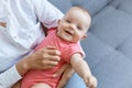 Close up portrait of cute charming baby in mother hands, unknown woman wearing white sitting on sofa with her smiling toddler