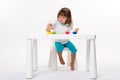 Close-up portrait of a cute cheerful little girl draws her own hands with gouache or finger paints at the table isolated on white Royalty Free Stock Photo