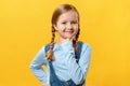Close-up portrait of a cute, curious, smart, attractive, little girl touching her chin, on a yellow background