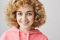 Close-up portrait of cute feminine caucasian girl with frizzle hairstyle smiling broadly while standing against gray