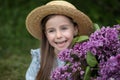 Close up portrait cute healthy joyful cheerful little Caucasian girl enjoying good mood. Smiling girl in straw hat with Lilac flow Royalty Free Stock Photo