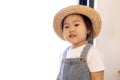 A close-up portrait of a cute little Asian girl. Funny Korean toddler in a straw hat, white T-shirt and denim jumpsuit at home Royalty Free Stock Photo