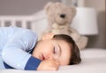 Close up portrait of cute little baby boy in light blue pajamas sleeping peacefully on bed at home with soft teddy bear toy at bac Royalty Free Stock Photo