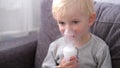 Close up portrait of cute little blond boy spraying respiratory diseases at home