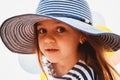 Close up portrait of cute little girl with big brown eyes in striped sunhat looking at camera Royalty Free Stock Photo