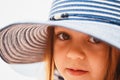 Close up portrait of cute little girl with big brown eyes in striped sunhat looking at camera. Selective focus Royalty Free Stock Photo
