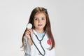 Close-up portrait of cute little girl, child in image of doctor wearing white lab coat with stethoscope isolated on