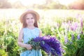 Close-up portrait of cute little girl in a hat with a bouquet of lupins in sunlight. Girl holding a bouquet of purple flowers in a Royalty Free Stock Photo