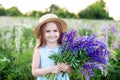 Close-up portrait of a cute little girl in a hat in a field of lupins. Girl holding a bouquet of purple flowers in the background Royalty Free Stock Photo