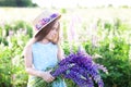 Close-up portrait of a cute little girl in a hat in a field of lupins. Girl holding a bouquet of purple flowers in the background Royalty Free Stock Photo