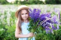 Close-up portrait of cute little girl in a hat in a field of lupins. Girl holding a bouquet of purple flowers in background of a f Royalty Free Stock Photo