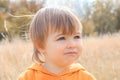 Close up portrait of cute little thoughtful baby boy gazing into the distance in autumn field.