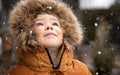 Close up portrait of cute little toddler boy in furry hood looking up at snowfall outdoors. Royalty Free Stock Photo