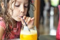 Close-up portrait of a cute little white Caucasian girl drinking a glass of fresh orange juice Royalty Free Stock Photo