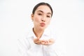 Close up portrait of cute office lady sends air kiss on palms, puckers lips and looks tender at camera, stands over Royalty Free Stock Photo