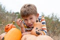 Close-up portrait of cute preschooler boy sitting in field near big pumpkins decorated for Halloween. October, outdoor. Harvesting Royalty Free Stock Photo