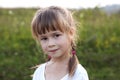 Close-up portrait of cute pretty child girl with gray eyes and long fair hair braids smiling shyly on blurred sunny summer green