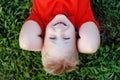 Portrait of cute smiling blonde little boy with blue eyes , wear red shirt lying on grass in park looking at camera. Royalty Free Stock Photo