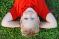 Close up portrait of cute smiling little boy with blue eyes , wear red shirt lying on grass in park looking at camera. Royalty Free Stock Photo