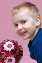 Close up portrait of cute smiling sly baby boy in blue sweater on pink background with pretty bouquet of flowers, looking right in Royalty Free Stock Photo