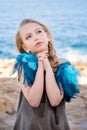 Close-up portrait of a cute young blond girl making a wish with hands clasped in fists in a dreamy pose on the sea