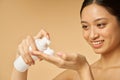 Close up portrait of cute young woman smiling, holding a bottle of gentle foam facial cleanser isolated over beige Royalty Free Stock Photo