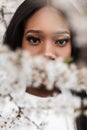 Close-up portrait of a delightful young black woman with an amazing look at the camera near the flowers. Pretty girl with an Royalty Free Stock Photo