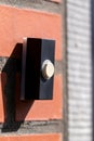 A close up portrait of a doorbell on a red brick wall. The device is next to a door and is black with a white button to be pressed Royalty Free Stock Photo