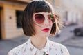 Close-up portrait of dreamy white woman with short hair standing on the street. Outdoor photo of pleasant caucasian