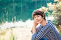 Close up portrait of dreamy woman sitting on lakeside and enjoying beautiful serene day looking at lake and forest. Idyllic calm