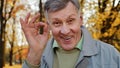 Close-up portrait elderly man positive grandpa showing consent sign looking at camera in autumn park smiling happily Royalty Free Stock Photo