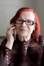 Close-up portrait of elderly woman with red hair, wearing eyeglasses. grandmother calls on phone, waits for an answer, listens,