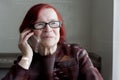 Close-up portrait of elderly woman with red hair, wearing eyeglasses. Sad grandmother calls on phone, waits for an answer, listens