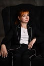 Close up portrait of elegant young lady with red hair dressed in black posing in darkness at high armchair thoughtfully looking Royalty Free Stock Photo