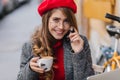 Close-up portrait of emotional french woman in glasses drinking latte on the street. Adorable long-haired girl in red Royalty Free Stock Photo