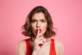 Close-up portrait of emotional pretty brunette woman showing silence gesture, looking at camera