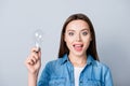Close up portrait of emotional smart cheerful girl in jeans shirt holding a light bulb, founded a great, new solution while stan Royalty Free Stock Photo