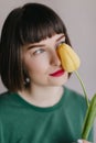 Close-up portrait of enchanting brunette female model in green attire sniffs tulip. Studio shot of carefree woman with Royalty Free Stock Photo